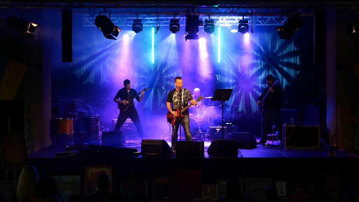 Gitarzysta z zespołem na scenie Ośrodka Kultury, W tle kolorowe światła