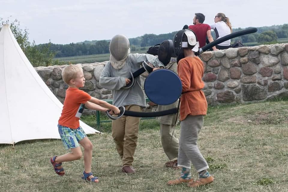 dzieci w hełmach rycerskich walczą na piankowe miecze