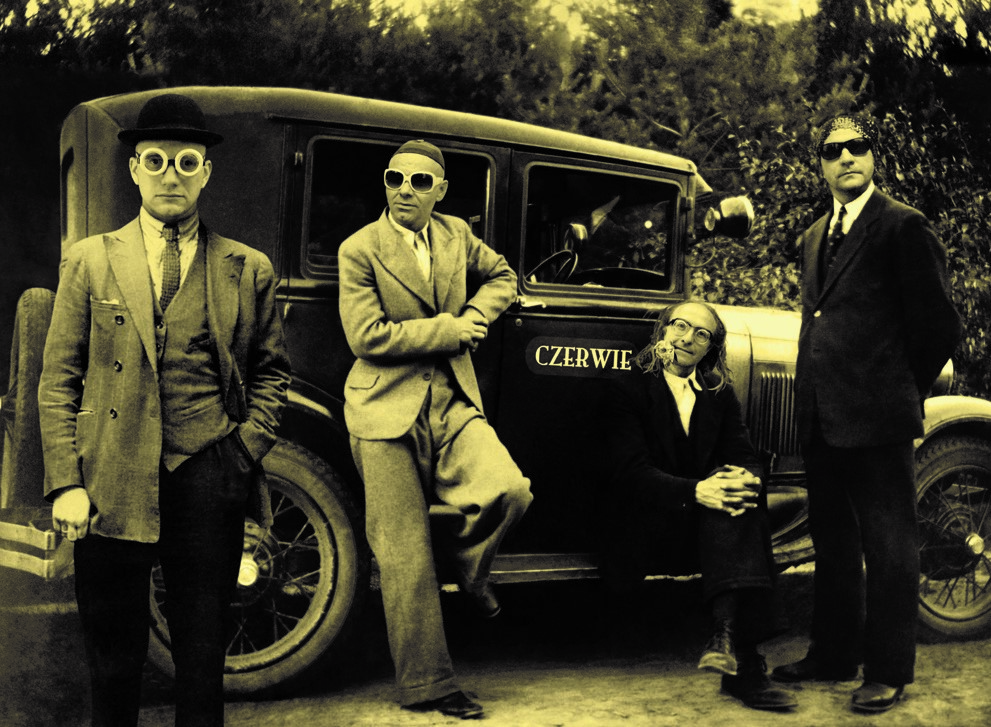 zdjęcie sepia przedstawiające członków grupy czerwie ubranych w garnitur na tle samochodu z XX wiekuzdjęcie sepia przedstawiające członków grupy czerwie ubranych w garnitur na tle samochodu z XX wieku